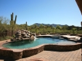 Raised pool and spa with rock waterfall — custom design by True Blue Pools